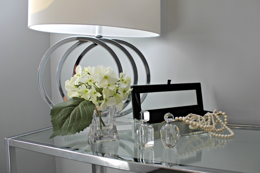 staged glass table with a lamp, perfume and pearls